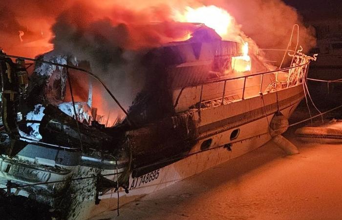 Beeindruckender Brand auf einem Boot mitten in der Nacht in einem Hafen, Eindämmungsmaßnahmen wurden durchgeführt, um jegliches Risiko einer Verschmutzung zu vermeiden